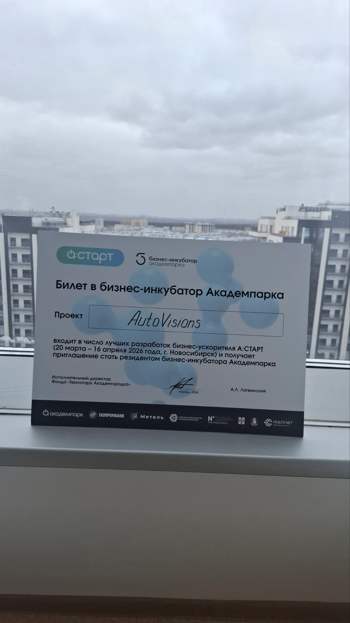 Билет в бизнес-инкубатор Академпарка с названием проекта AutoVisions на подоконнике, за окном Новосибирск